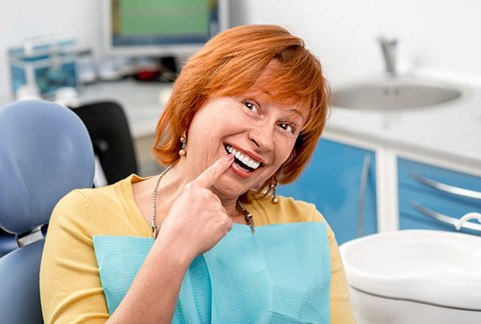 Woman in patient’s chair pointing at her dental implant