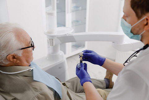 Dentist showing senior male patient a dental implant and crown