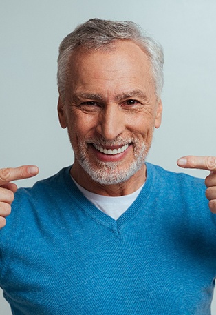 A handsome senior man pointing to his beautiful, well-fitted dentures