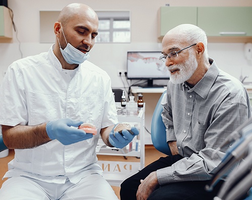 An older man talking to a dentist holding some dentures