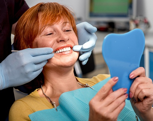 A smiling older woman admiring her dentures in a hand mirror